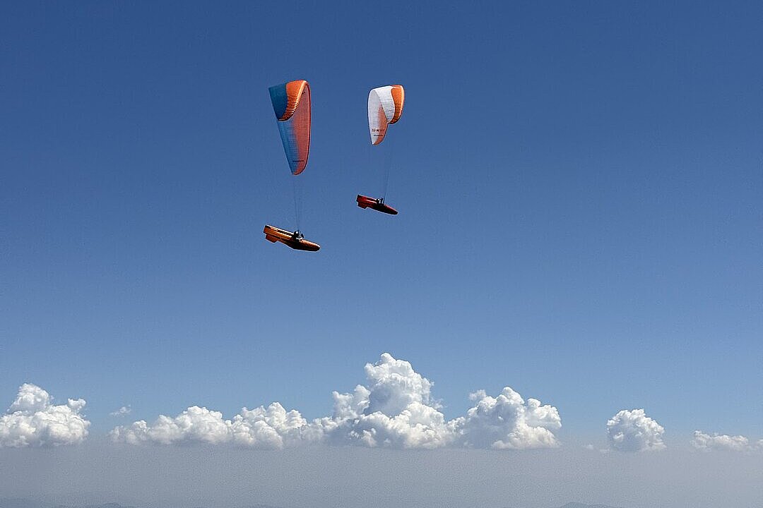 Zwei Gleitschirme mit Motoren fliegen nebeneinander am blauen Himmel.