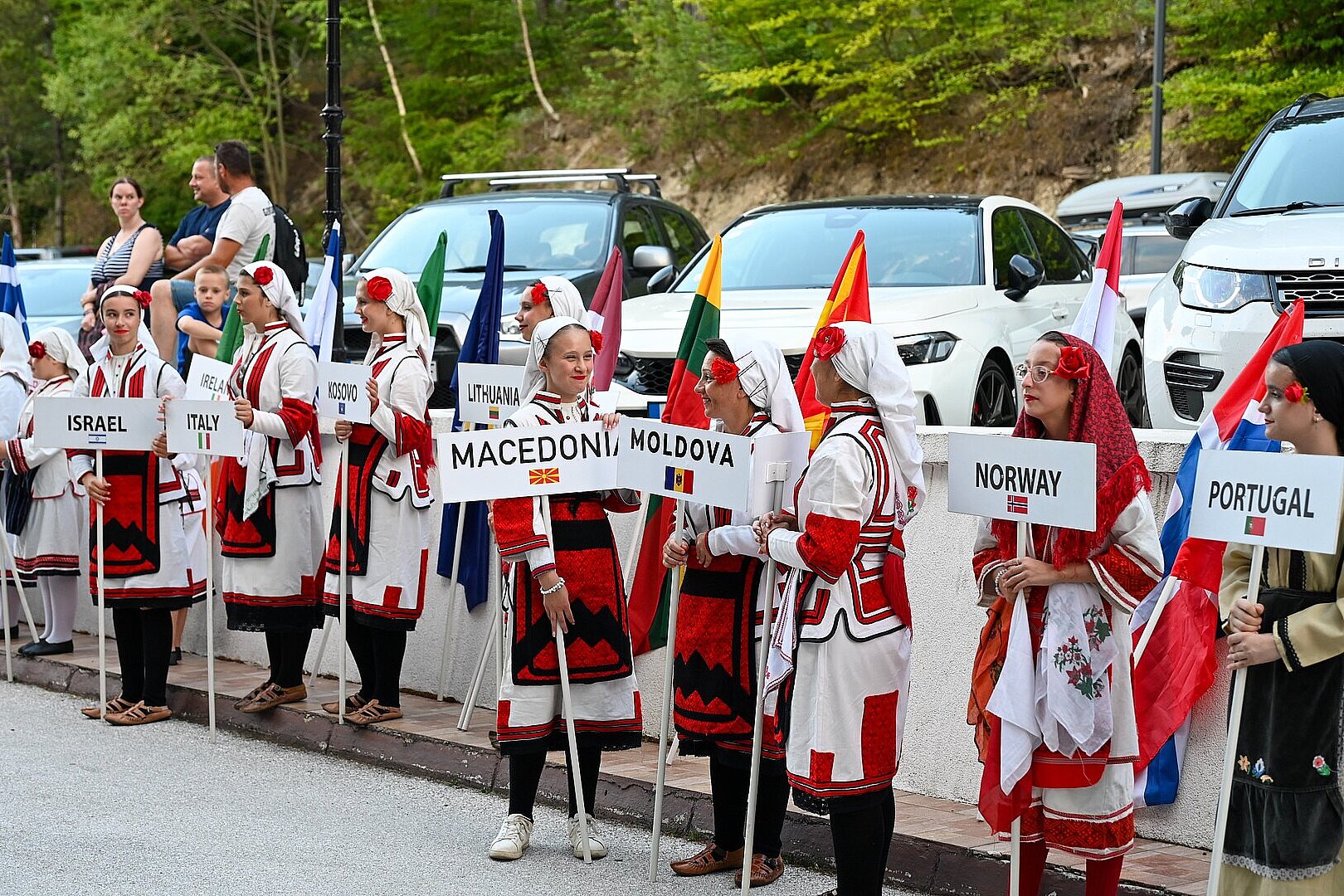 Menschen in traditioneller Kleidung tragen Schilder mit Ländernamen.