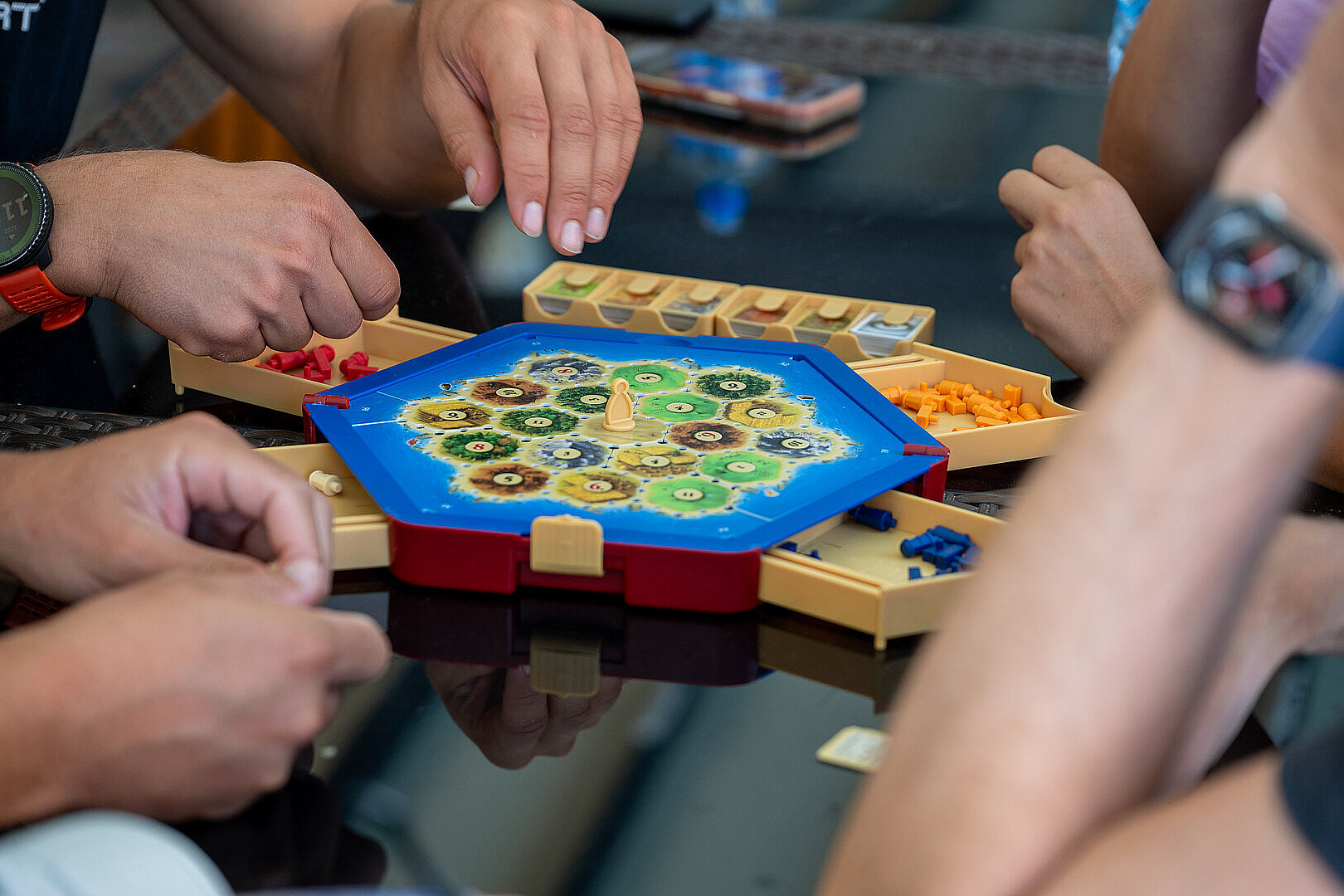 Mehrere Hände greifen nach Spielfiguren auf einem Brettspiel am Tisch