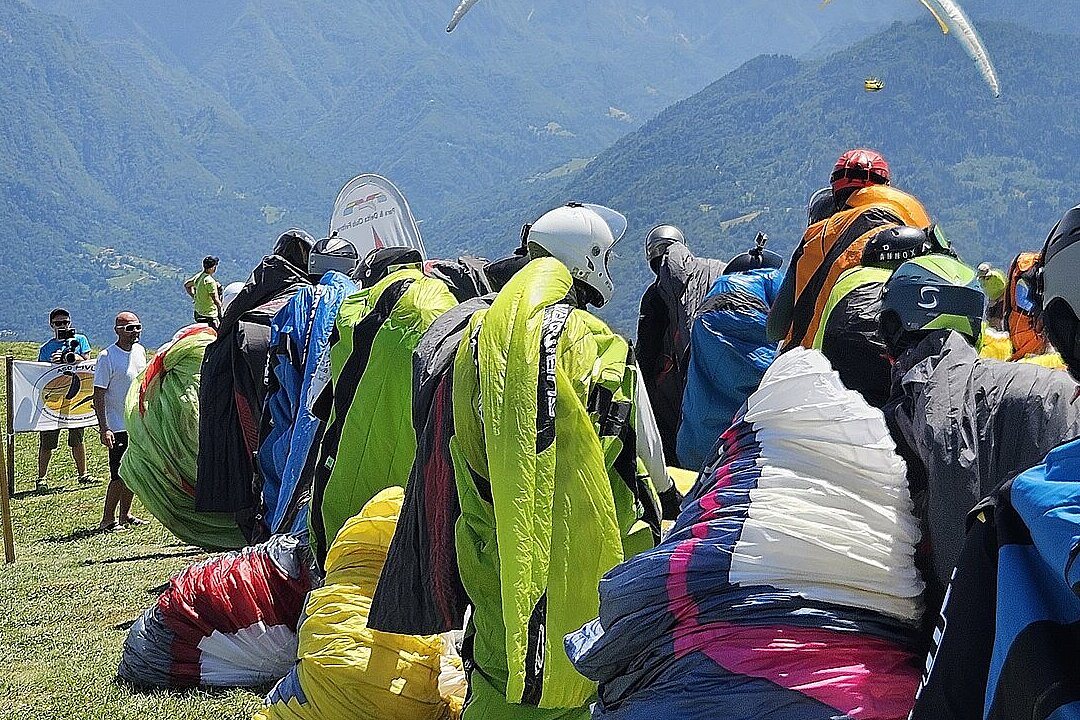 Piloten warten am Startplatz mit ausgebreiteten Gleitschirmen vor Bergkulisse.