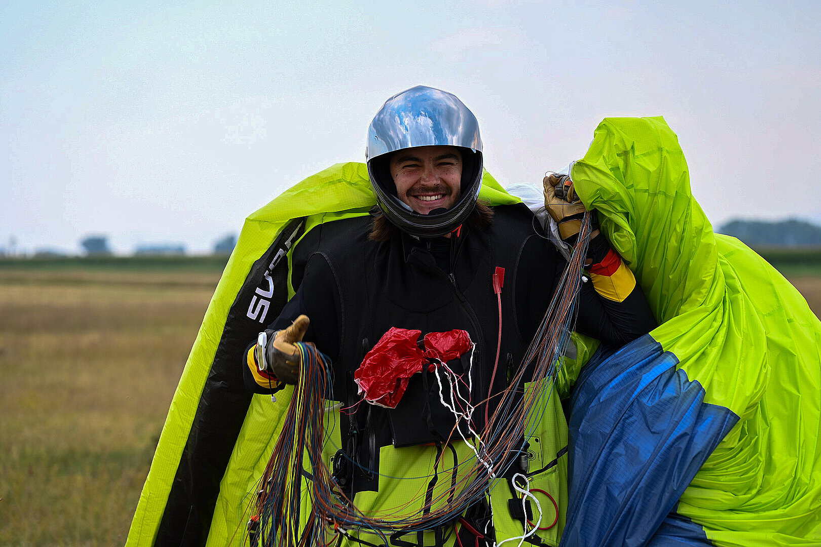 Pilot im Fluganzug lächelt mit Helm und Leinen in der Hand.