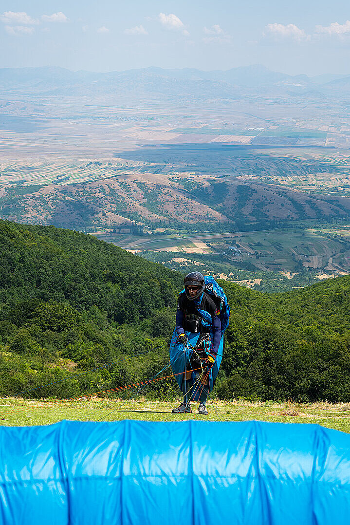 Pilot steht startbereit mit ausgelegtem Gleitschirm vor einer Berglandschaft.