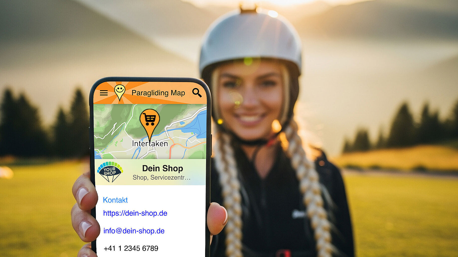 Frau mit Helm hält Smartphone mit Paragliding-Karten-App in die Kamera