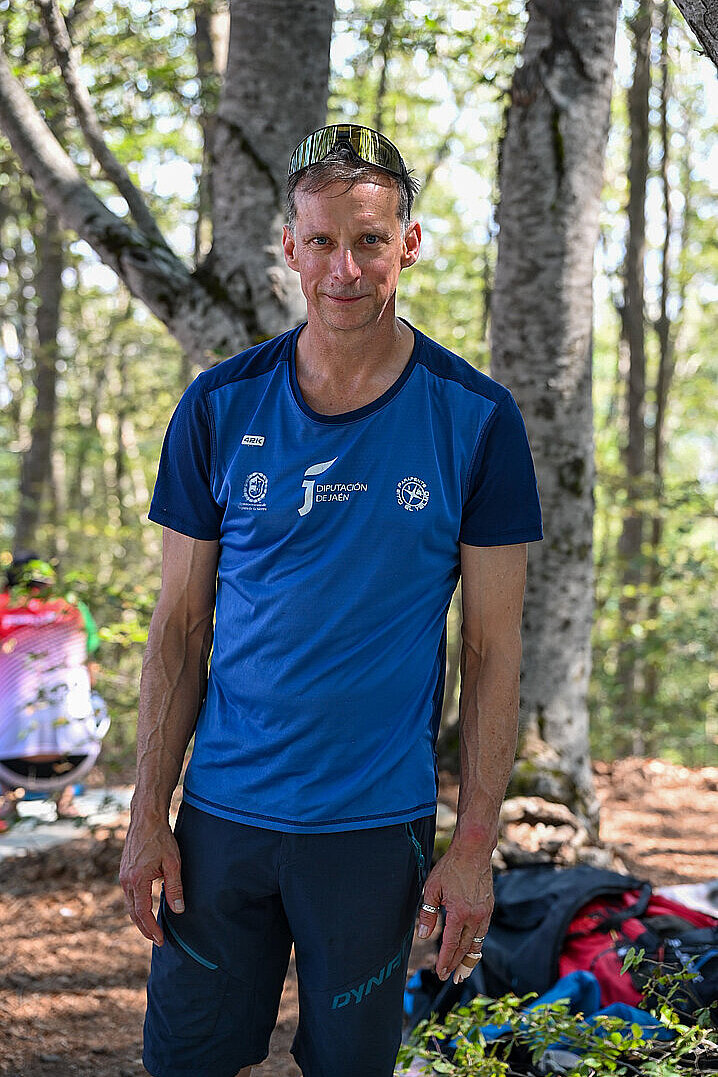 Mann in blauem Shirt steht im Wald, daneben liegen Gleitschirmausrüstung und Rucksack.
