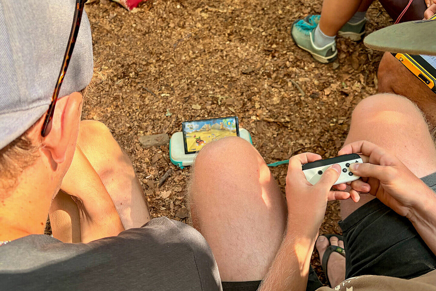 Mehrere Personen sitzen draußen und spielen mit einer Handheld-Konsole