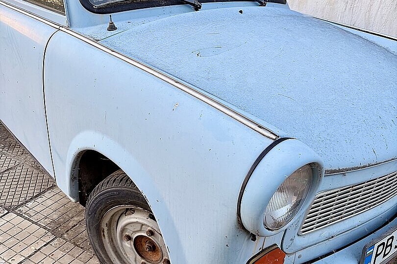 Ein hellblauer alter Kleinwagen steht am Straßenrand.
