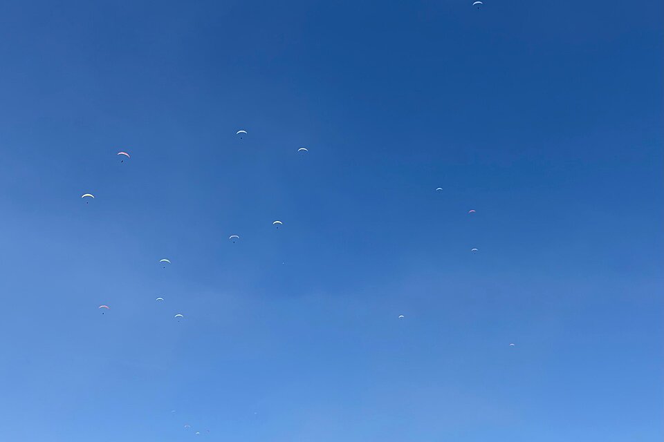 Mehrere Gleitschirme sind als kleine Punkte am blauen Himmel zu sehen.
