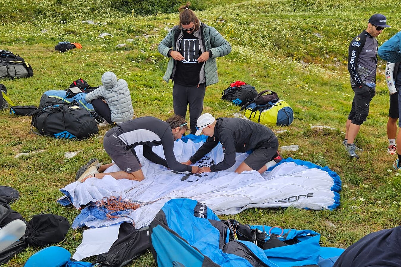 Zwei Personen richten gemeinsam einen ausgebreiteten Gleitschirm auf einer Wiese zurecht.