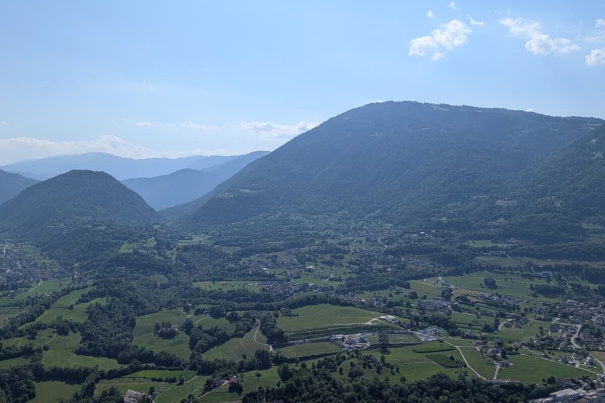 Blick aus der Luft über ein Tal mit Bergen und einzelnen Gleitschirmen.