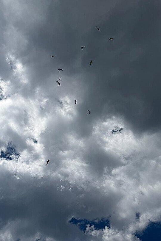 Mehrere Gleitschirme schweben vor dunklen Wolken am Himmel.
