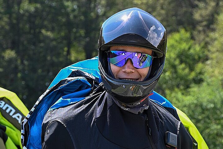 Pilot im Fluganzug und Helm hält Leinen und lächelt in die Kamera.