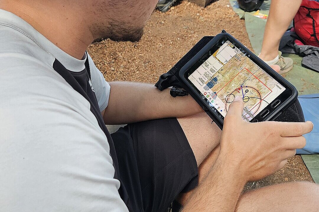 Mann sitzt am Boden und betrachtet ein Tablet mit Kartenansicht und Wegmarkierungen.