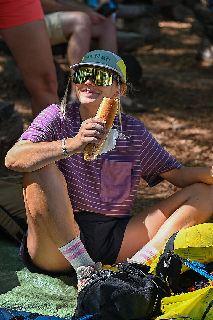 Frau sitzt im Schatten und isst ein Brötchen.