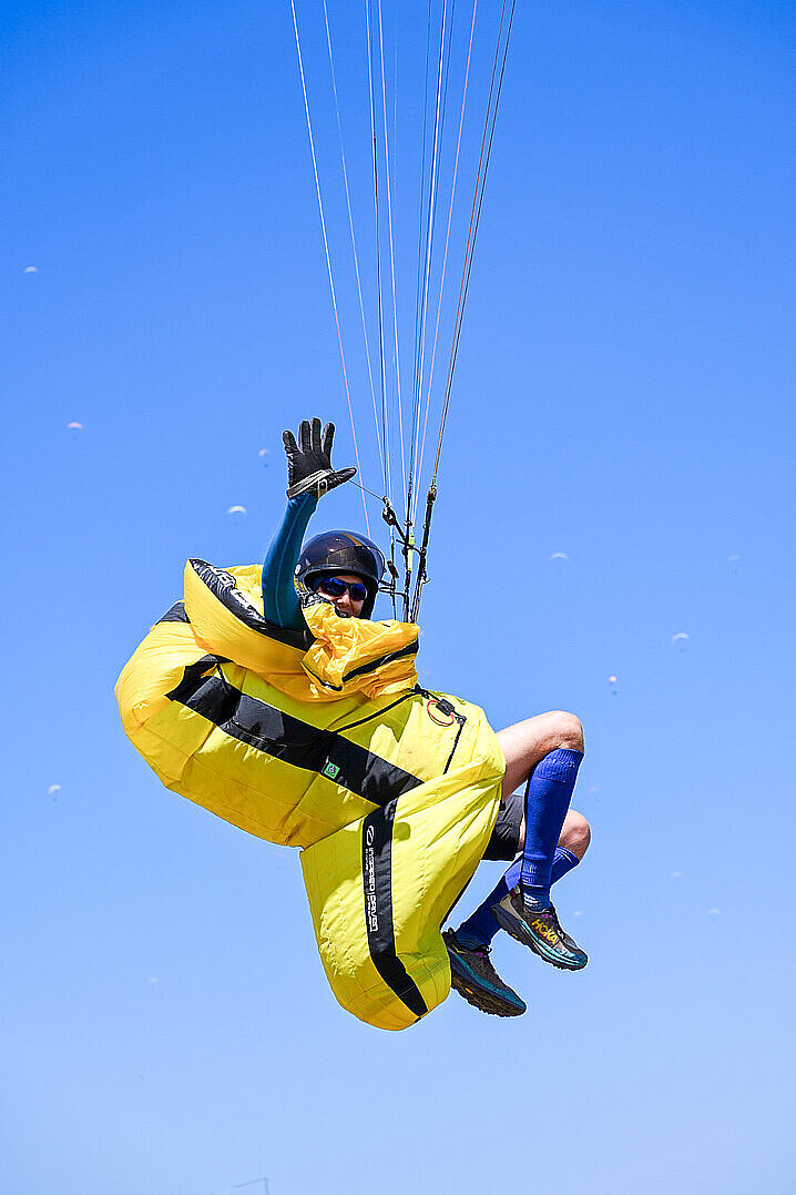 Ein Pilot im gelben Schirm winkt in der Luft.