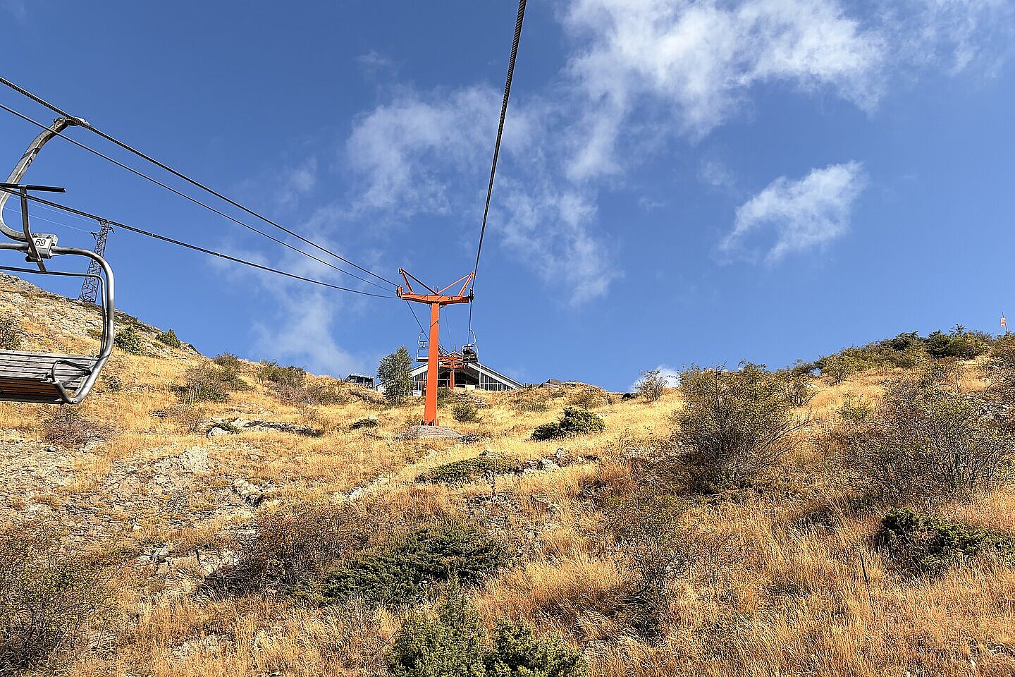Blick von einer Seilbahn über einen trockenen Hang mit Schienen und Himmel.