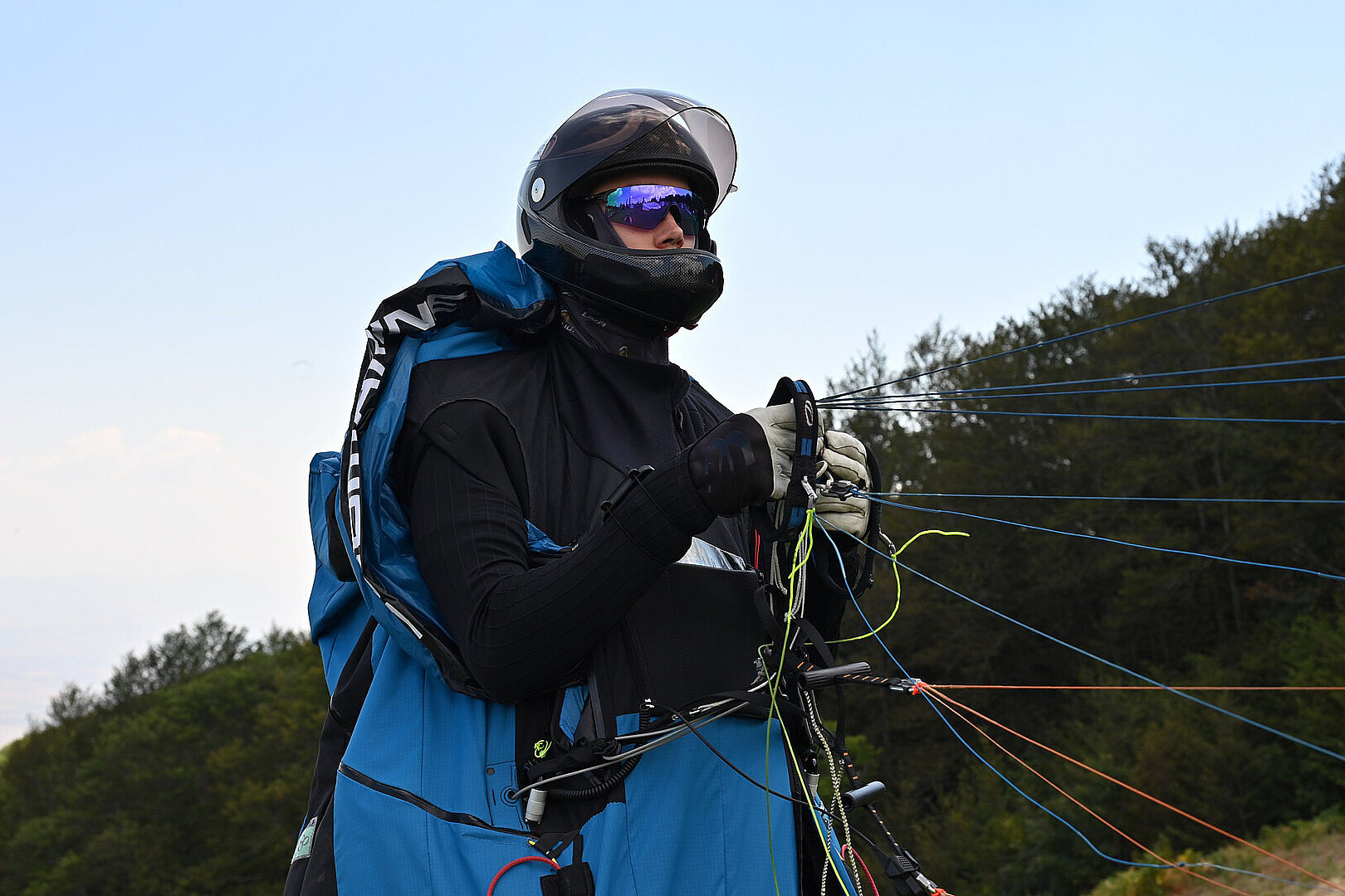 Pilot mit Helm und Handschuhen zieht Leinen auf einer Wiese.