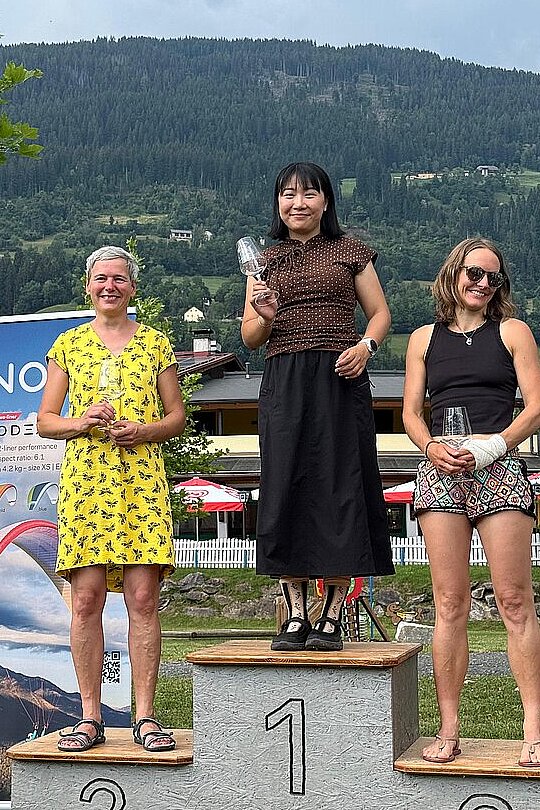 Drei Frauen auf dem Siegerpodest halten Gläser und kleine Pokale in der Hand.