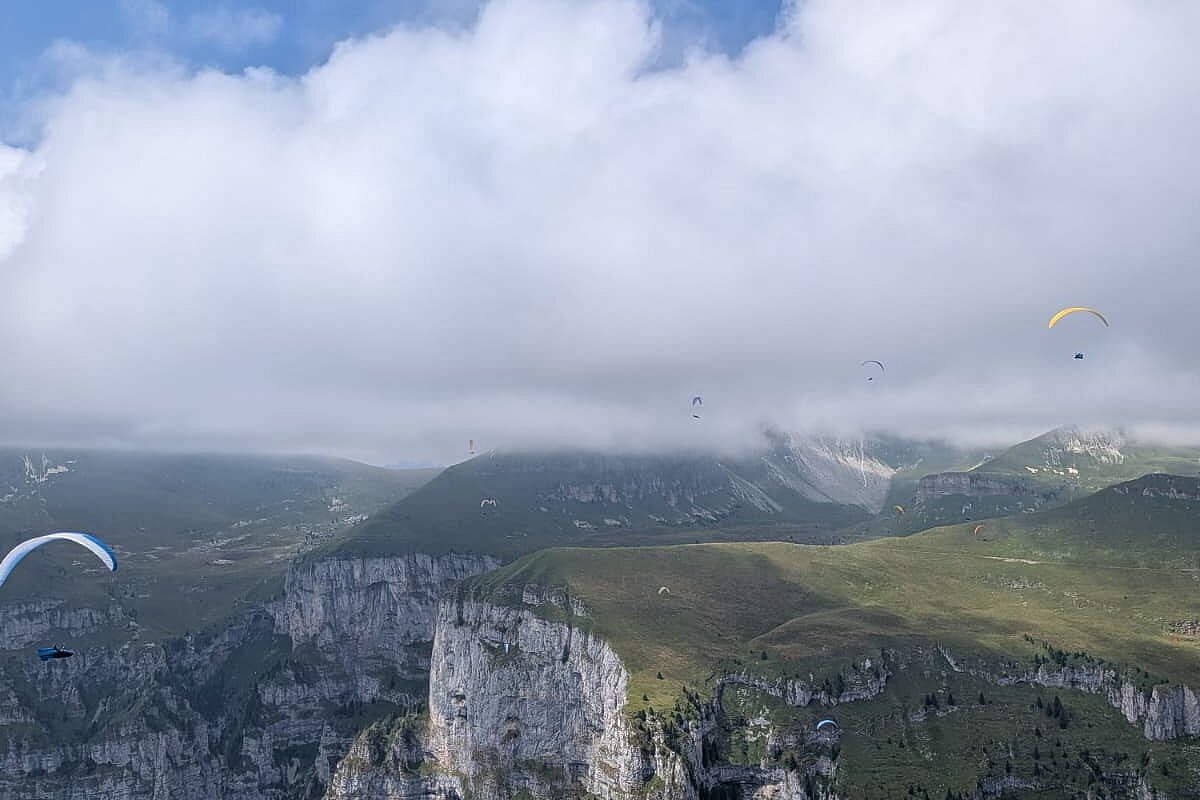 Gleitschirmflieger schweben über steilen Felsen und grünen Bergflächen.