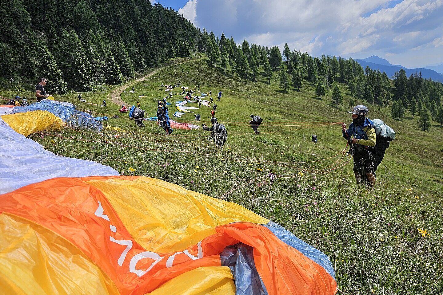 Pilotinnen und Piloten bereiten Gleitschirme auf einer Wiese am Hang vor.