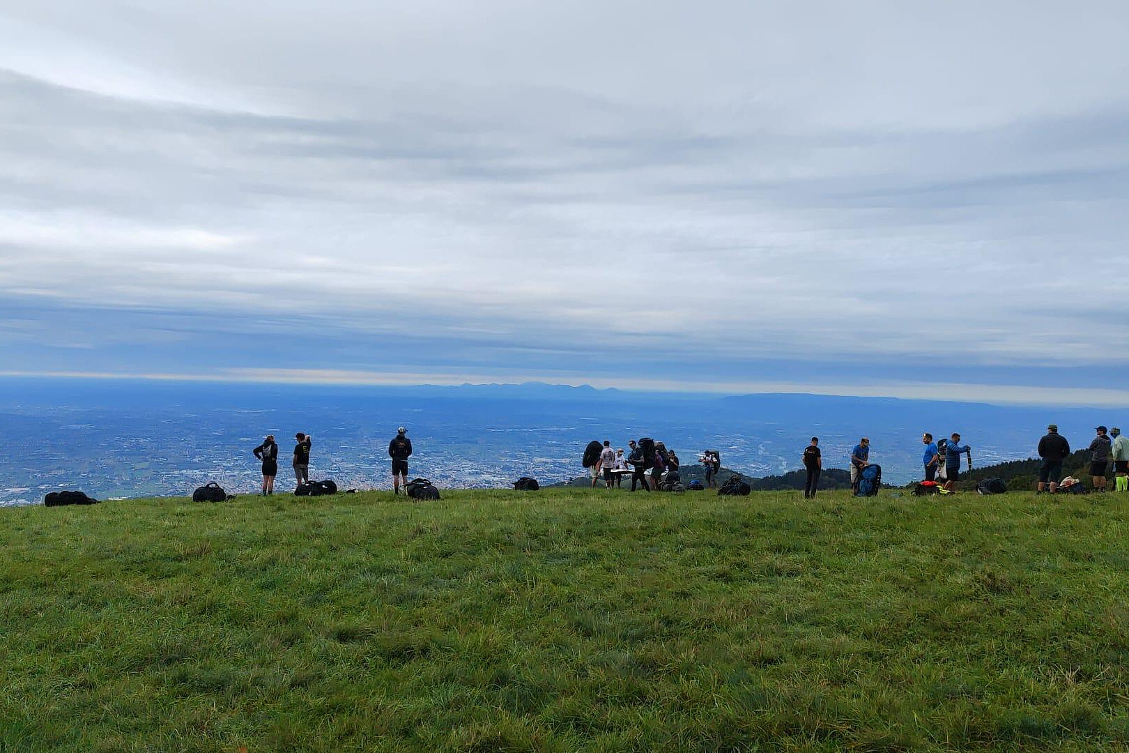 Mehrere Personen stehen auf einer Wiese am Startplatz und schauen ins Tal.
