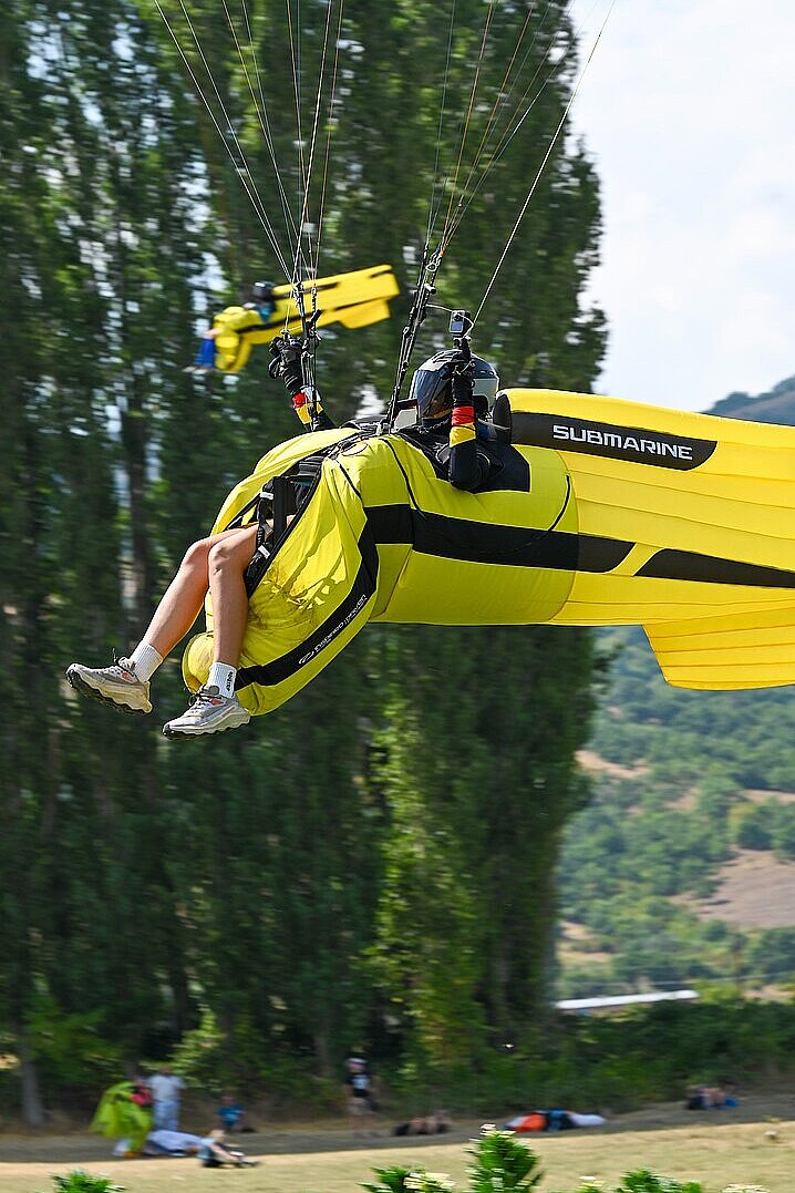 Gelb-violetter Gleitschirm schwebt mit Pilot über blauem Himmel.