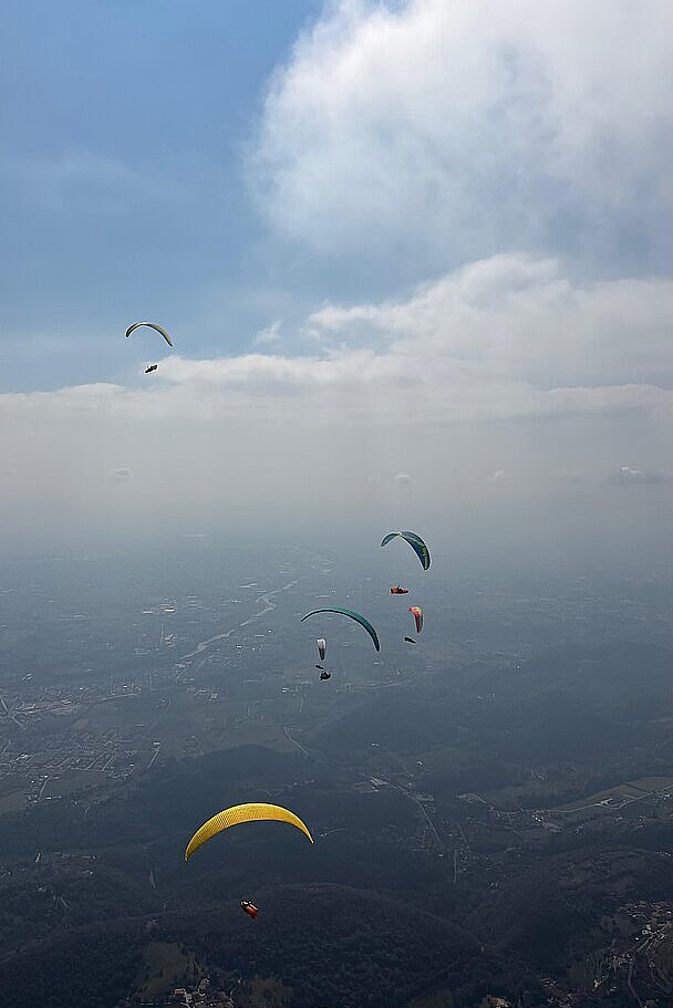 Mehrere Gleitschirme fliegen über einer hügeligen Landschaft in der Ferne.