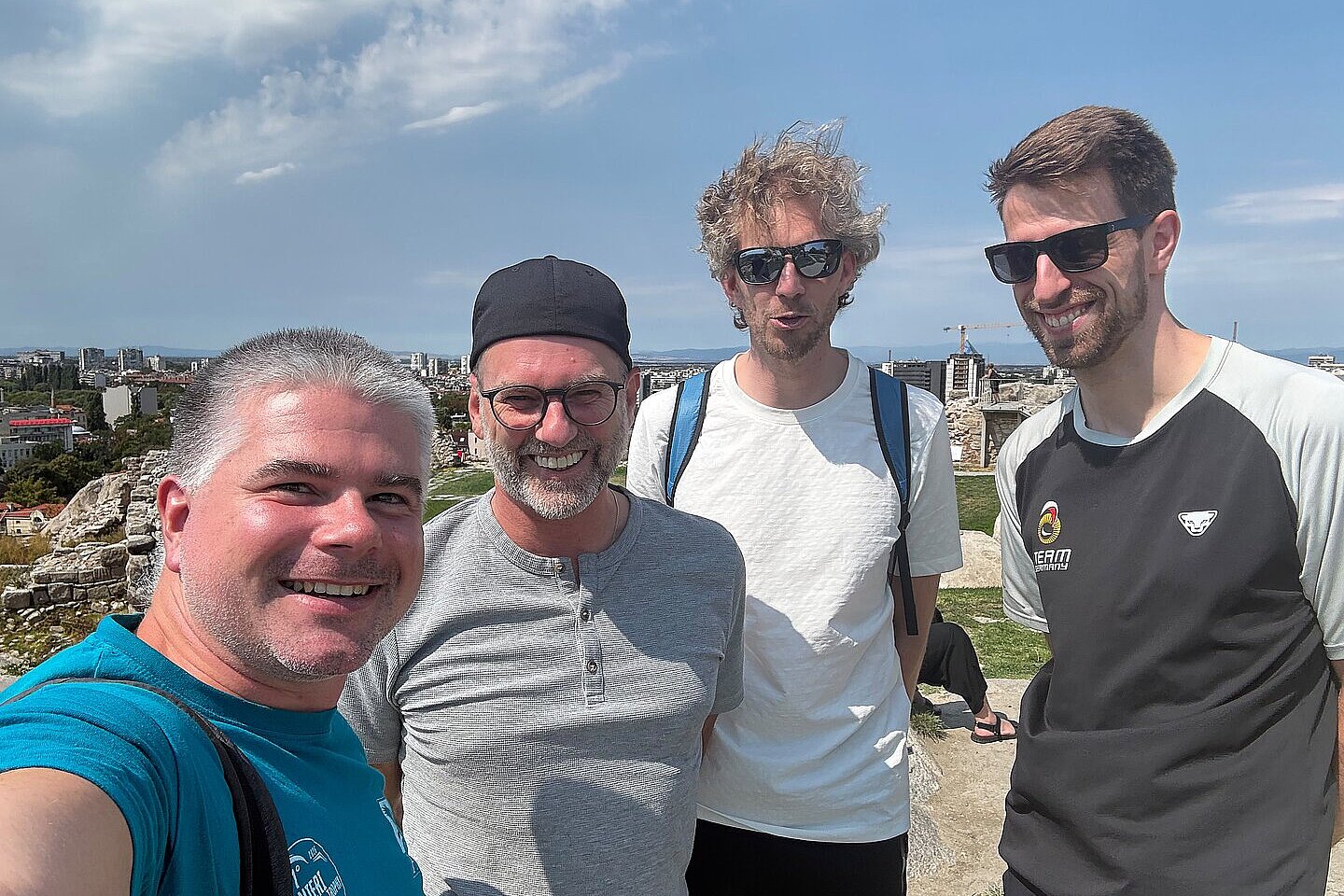 Vier Männer machen ein Selfie auf einer Anhöhe mit Stadtblick im Hintergrund.