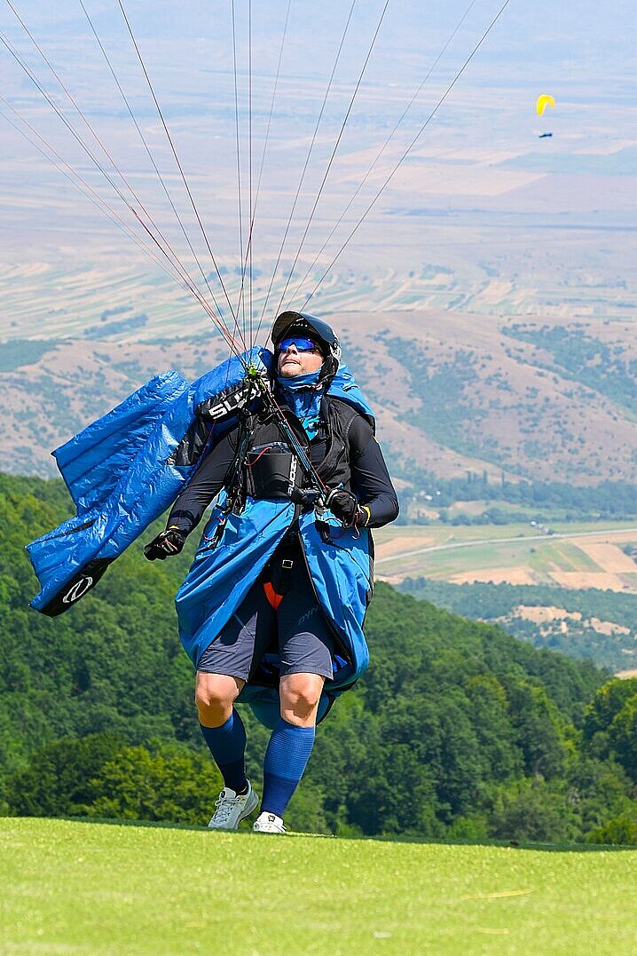 Pilot im Fluganzug steigt mit ausgelegtem Schirm zum Startplatz auf.