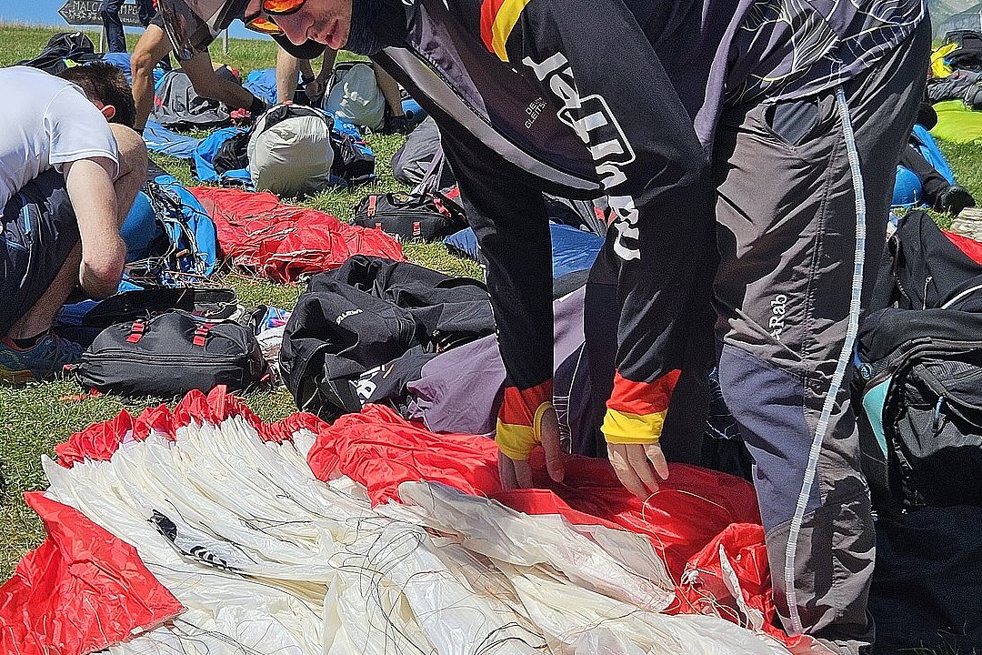 Pilot im Fluganzug kniet am Gleitschirm und sortiert die Leinen auf einer Wiese.