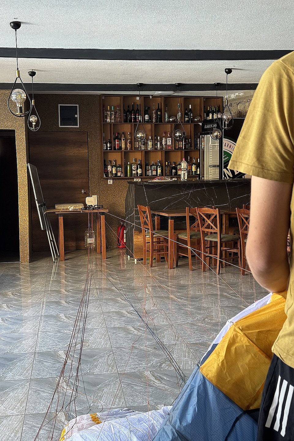 Mehrere Personen trimmen Gleitschirme in einem Innenraum neben einer Bar.