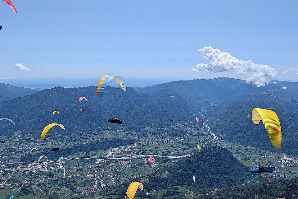 Gleitschirme über einem Tal mit Bergen, Fluss und verstreuten Wolken