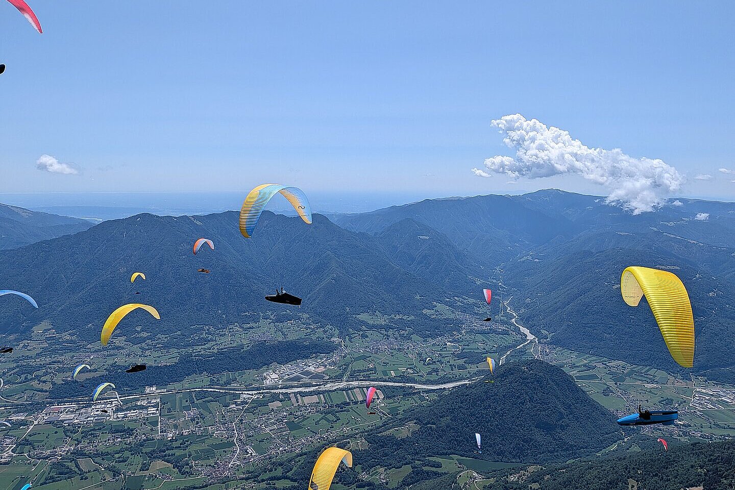 Gleitschirme über einem Tal mit Bergen, Fluss und verstreuten Wolken