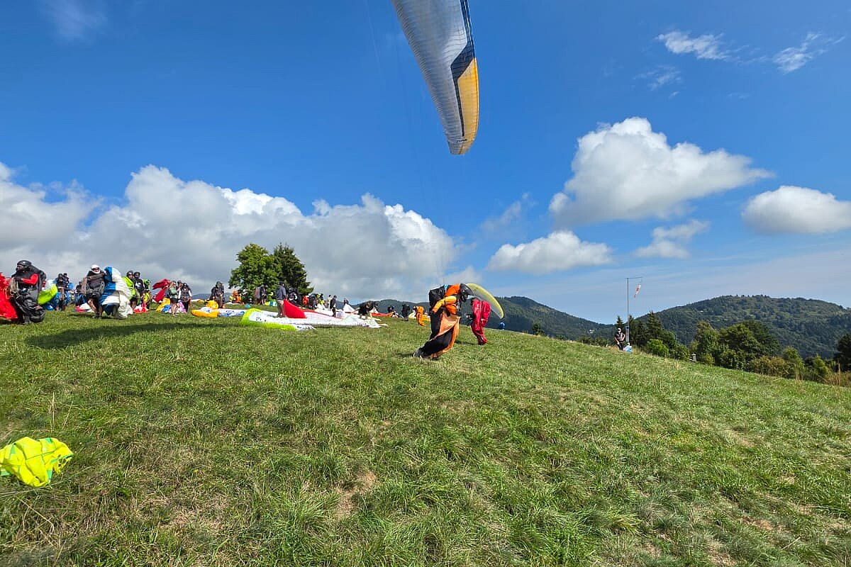 Auf einer Wiese bereiten mehrere Gleitschirmpiloten ihre Ausrüstung unter blauem Himmel vor.