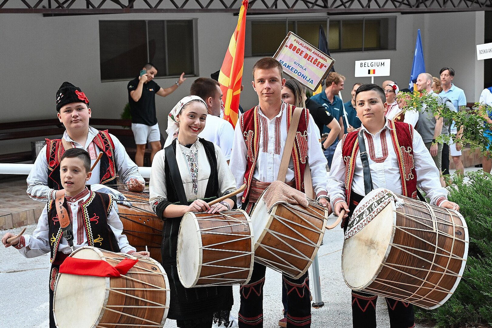 Personen in traditioneller Kleidung stehen mit Schildern und Fahnen an der Straße.