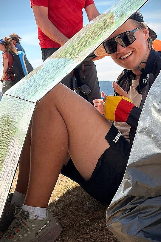Eine lächelnde Person sitzt unter einem Sonnenschutz am Startplatz.
