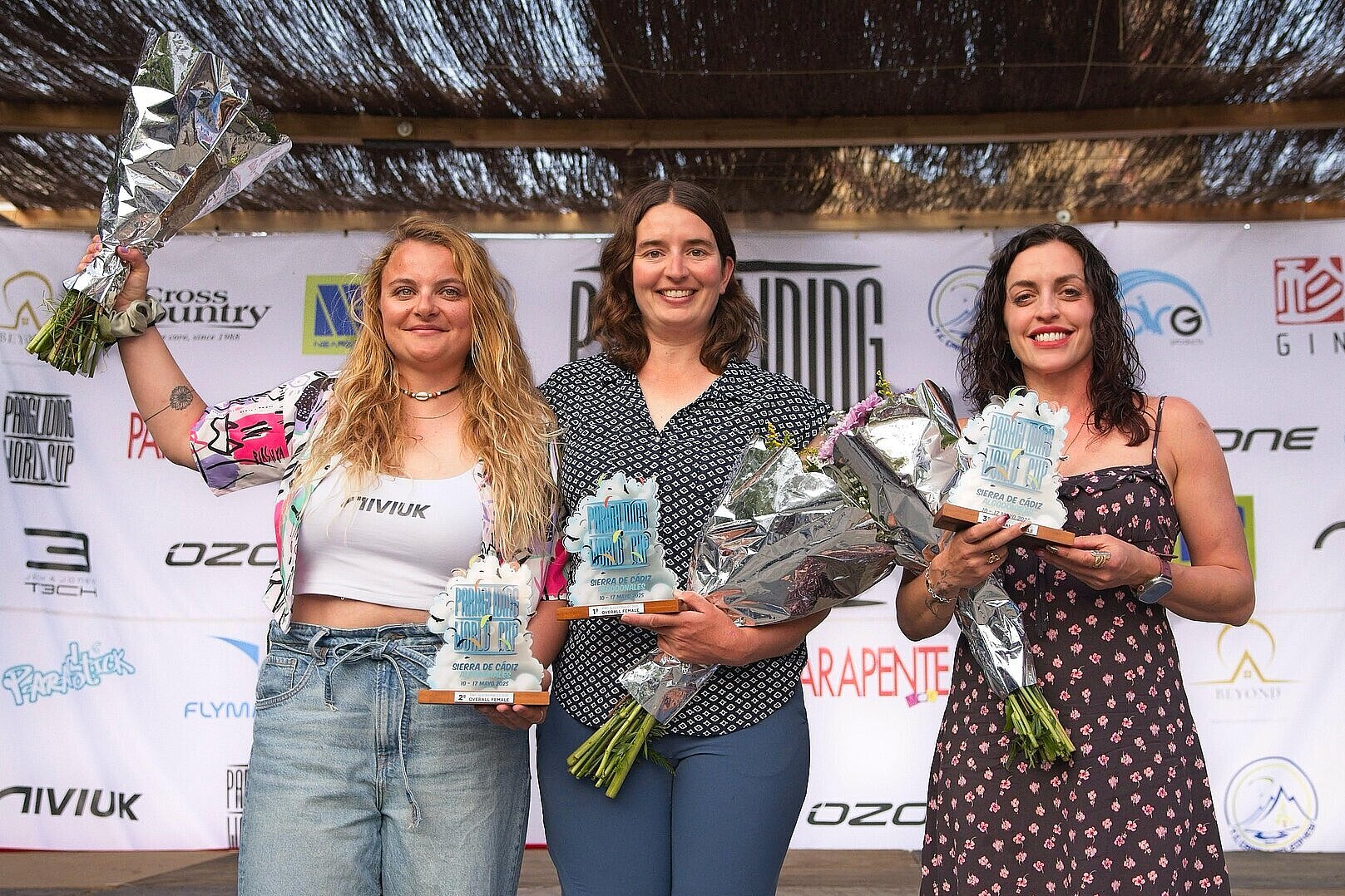 Drei Frauen stehen nebeneinander und halten Pokale und Blumen in ihren Händen
