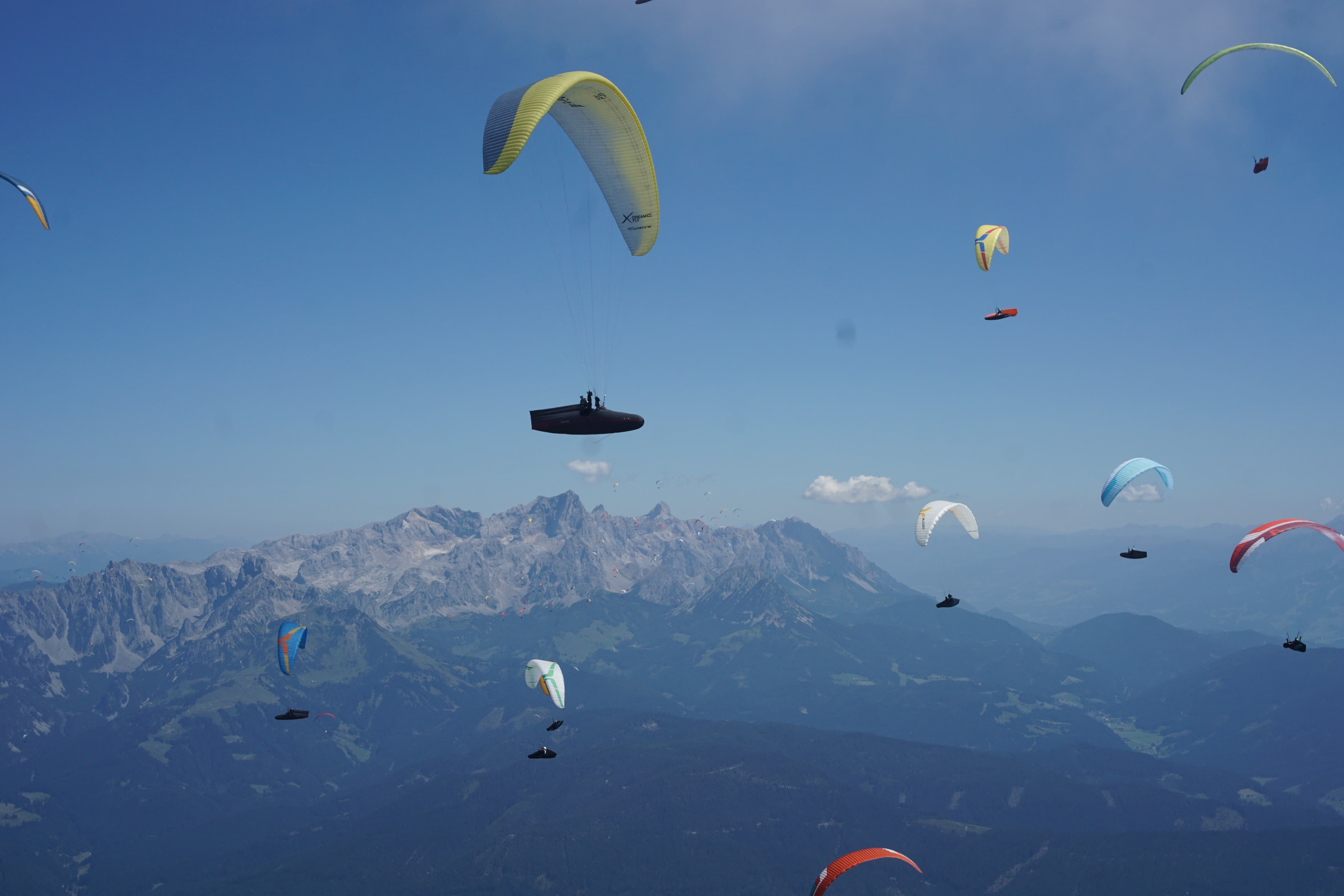 Mehrere Gleitschirme vor Bergkulisse mit wolkenlosem Himmel
