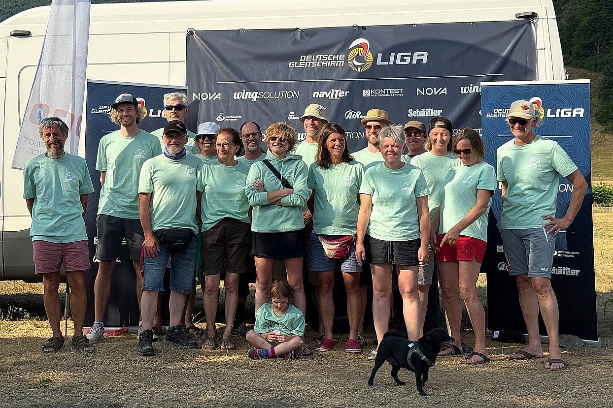Gruppe von Menschen in mintgrünen Shirts vor einem Banner und einem weißen Transporter, vorne ein kleiner schwarzer Hund.