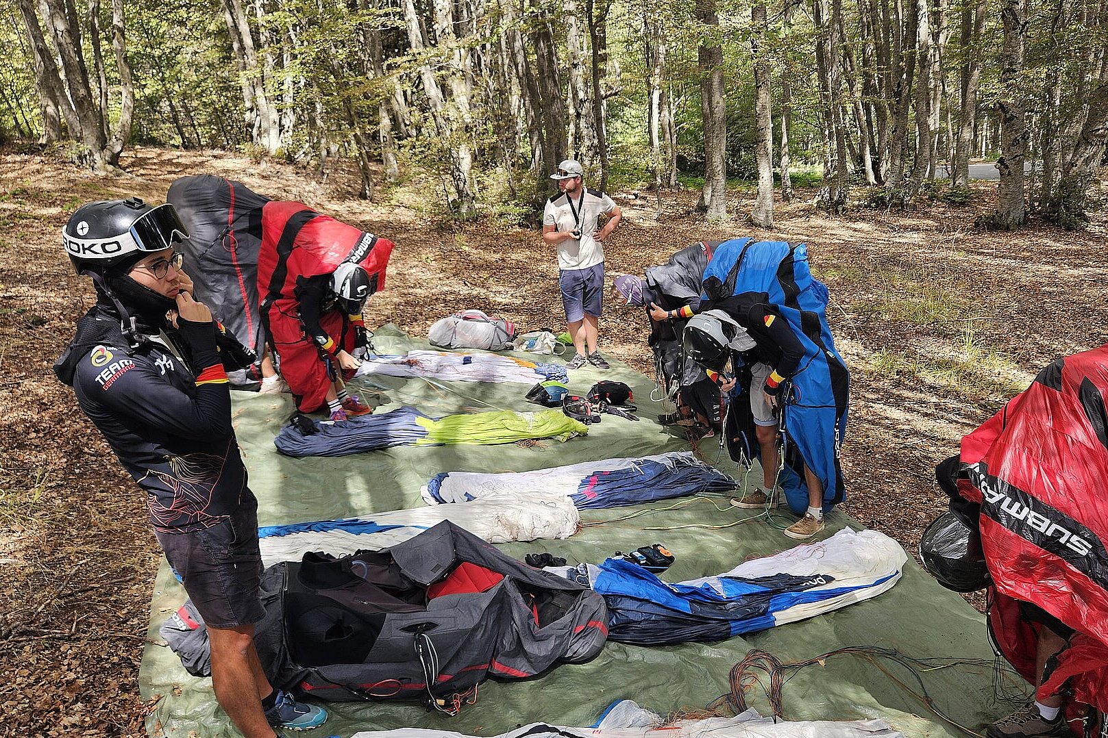 Mehrere Piloten packen ihre Gleitschirme auf einer Wiese aus.