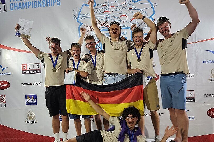 Sechs junge Männer mit Medaillen feiern auf dem Podest und halten eine Deutschlandflagge.