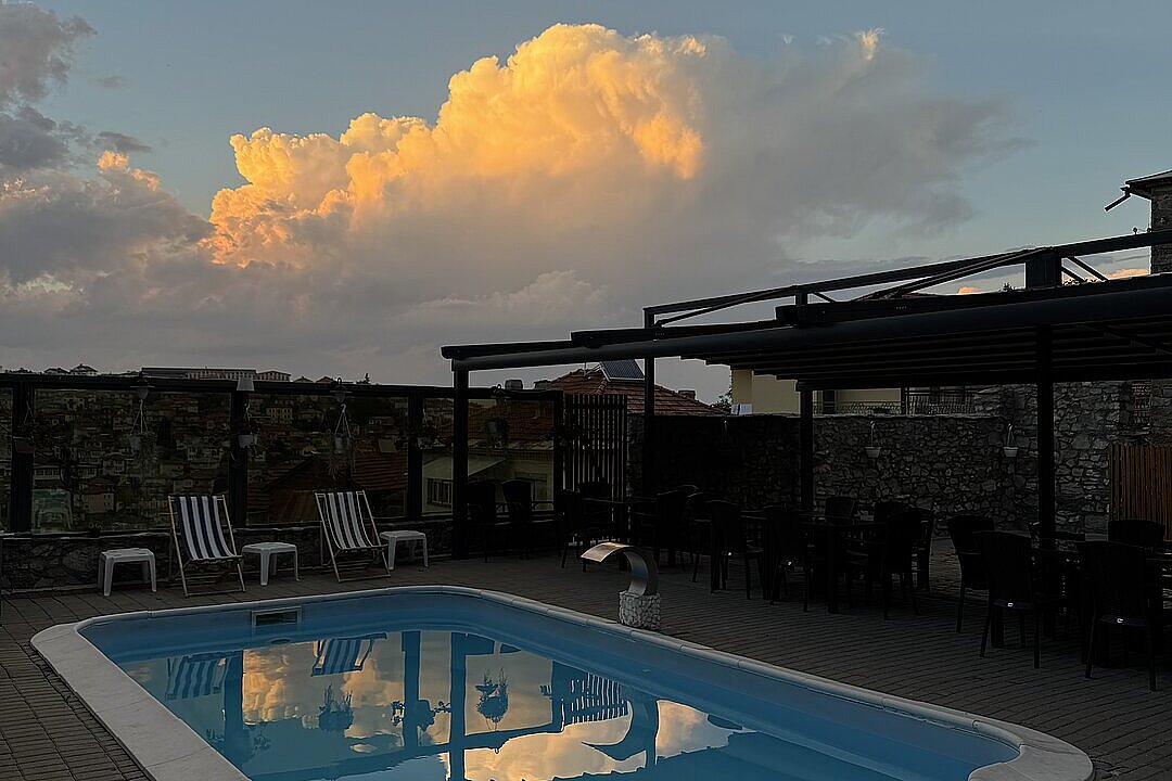 Leerer Pool im Innenhof, daneben Stühle und Tische unter einem Dach, Spiegelung der Wolken im Wasser.