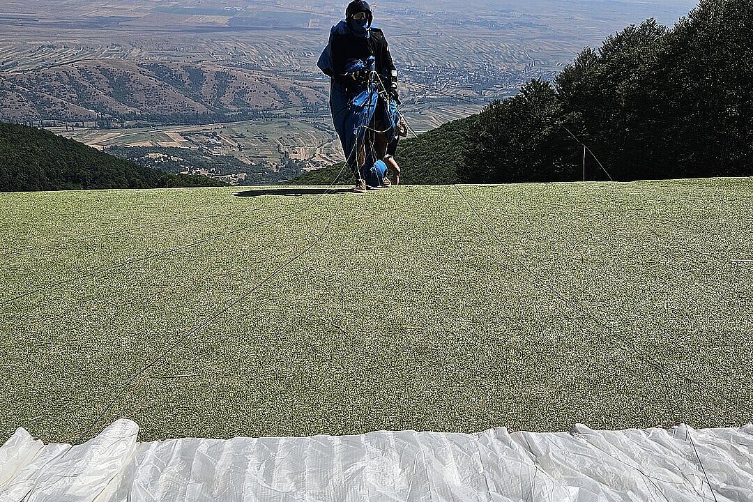 Pilot steht auf dem Startplatz vor weiter Landschaft und bereitet sich vor.