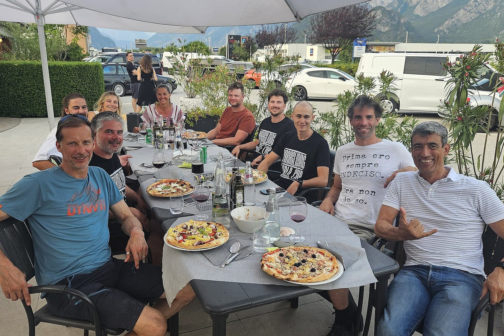 Mehrere Personen sitzen an einem Tisch im Freien und essen Pizza.