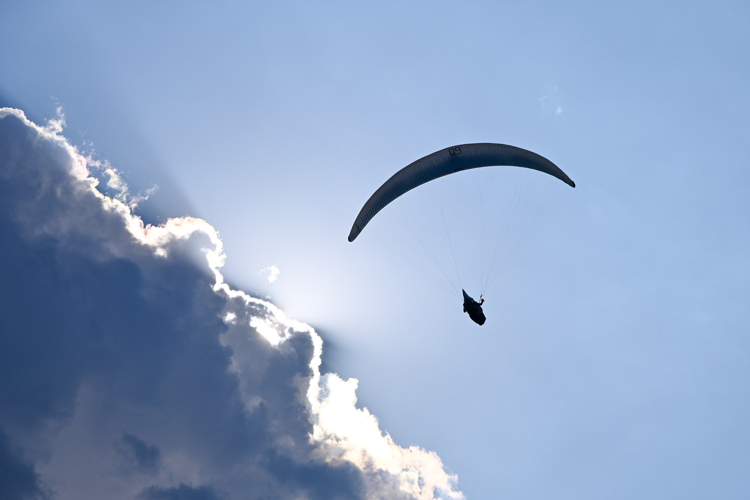 Ein Gleitschirm fliegt vor einer hellen Wolke am Himmel.