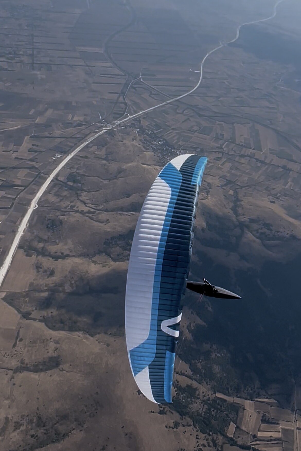 Mehrere Gleitschirme fliegen über einer Berg- und Tallandschaft.