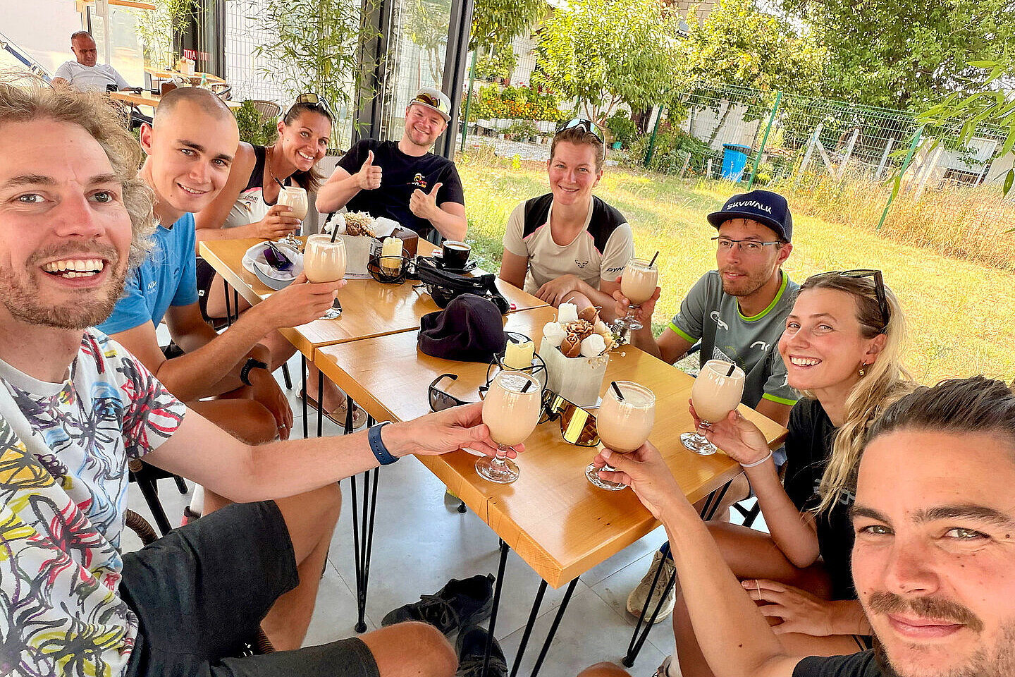 Gruppe sitzt an einem Tisch und stößt mit Getränken auf der Terrasse an