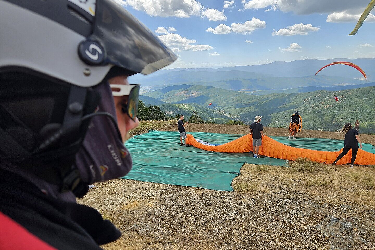 Ein Pilot im Helm steht mit aufgebautem Gleitschirm am Startplatz.