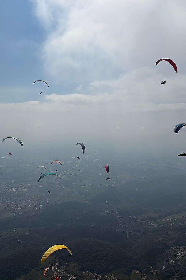 Mehrere Gleitschirmflieger am Himmel über einer bergigen Landschaft.