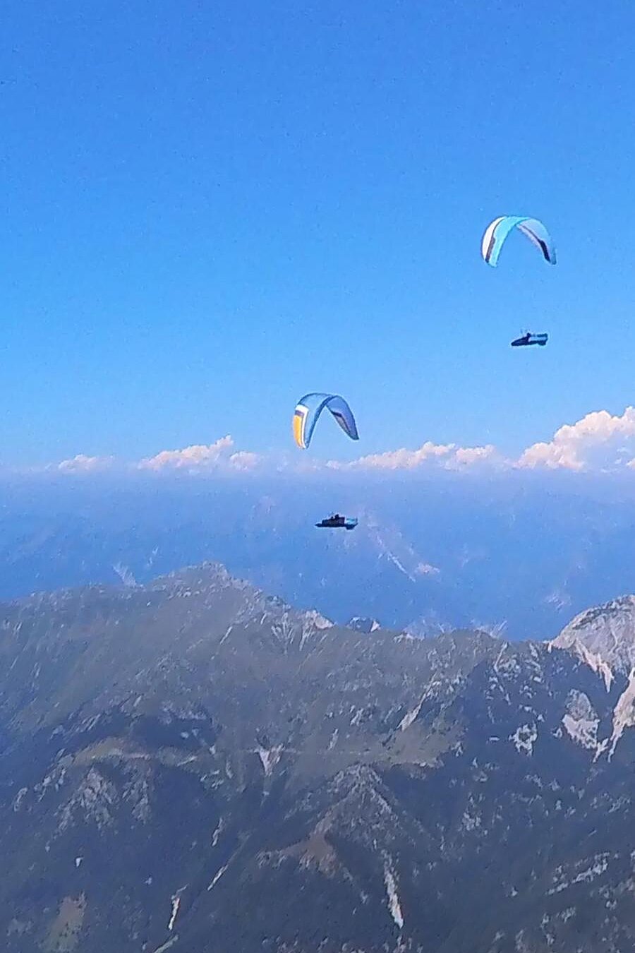 Drei Gleitschirme fliegen über Berglandschaft und Wolken.