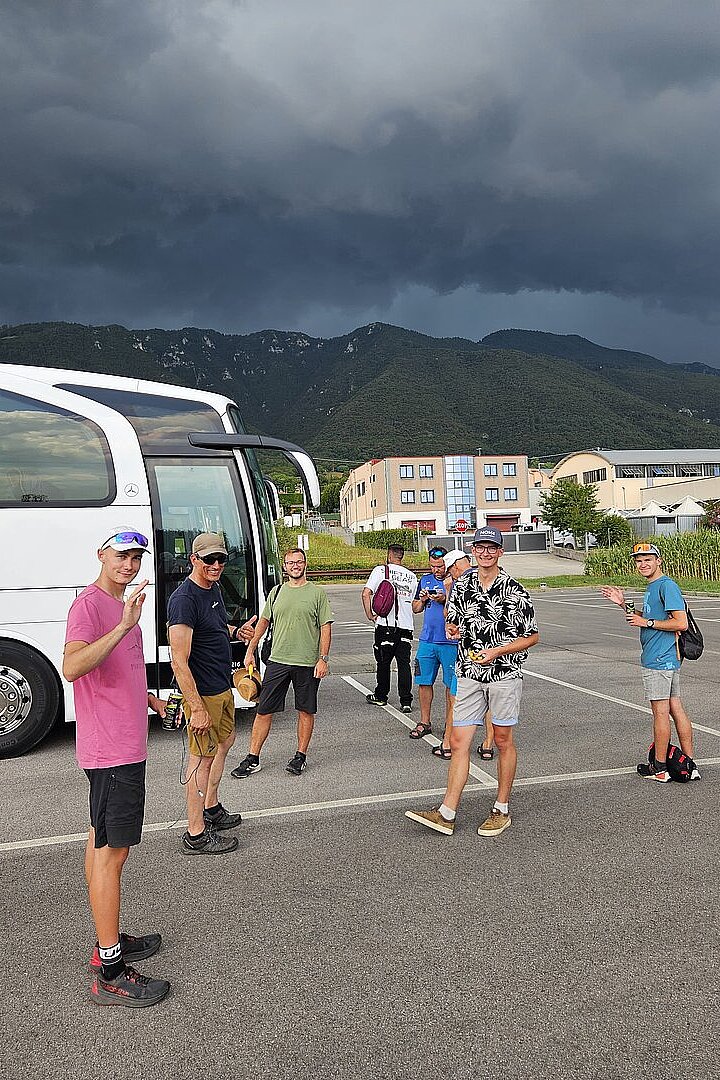 Mehrere Personen stehen neben einem Bus auf einem Parkplatz unter dunklen Gewitterwolken.